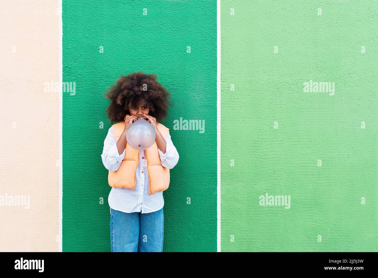 Mädchen bläst Ballon vor der grünen Wand stehen Stockfoto
