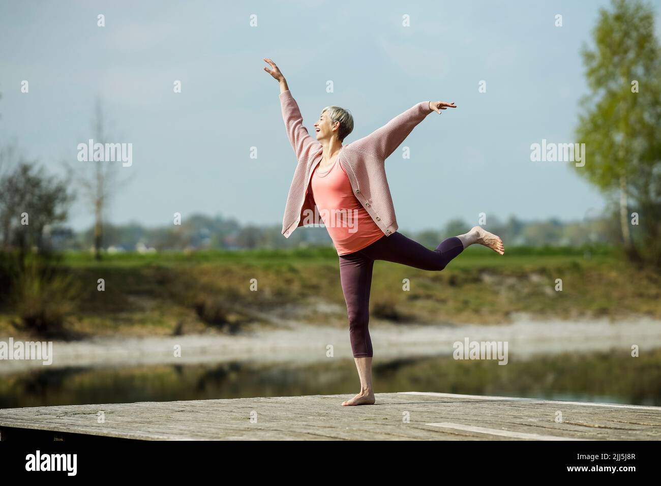 Glückliche reife Frau, die am Pier Gymnastik praktiziert Stockfoto