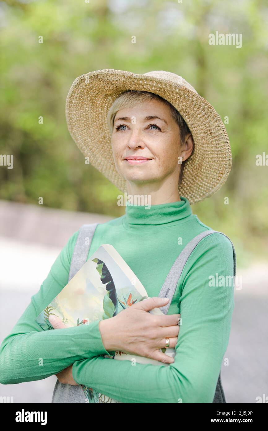 Nachdenkliche lächelnde Frau mit Hut und Buch Stockfoto
