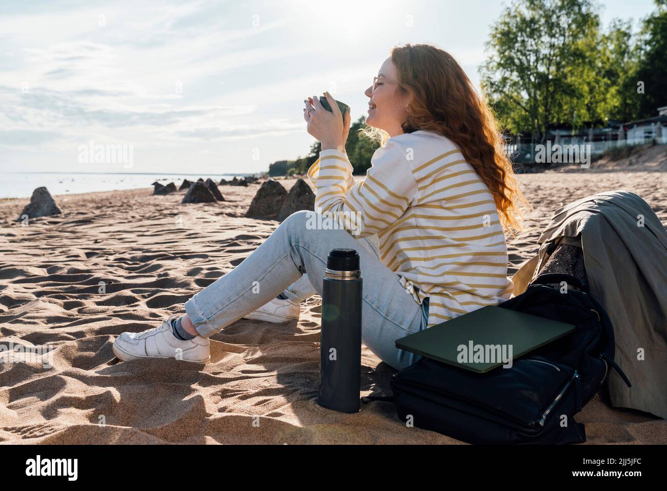 Lächelnde Frau, die am Strand in einer isolierten Tasse Kaffee trinkt Stockfoto