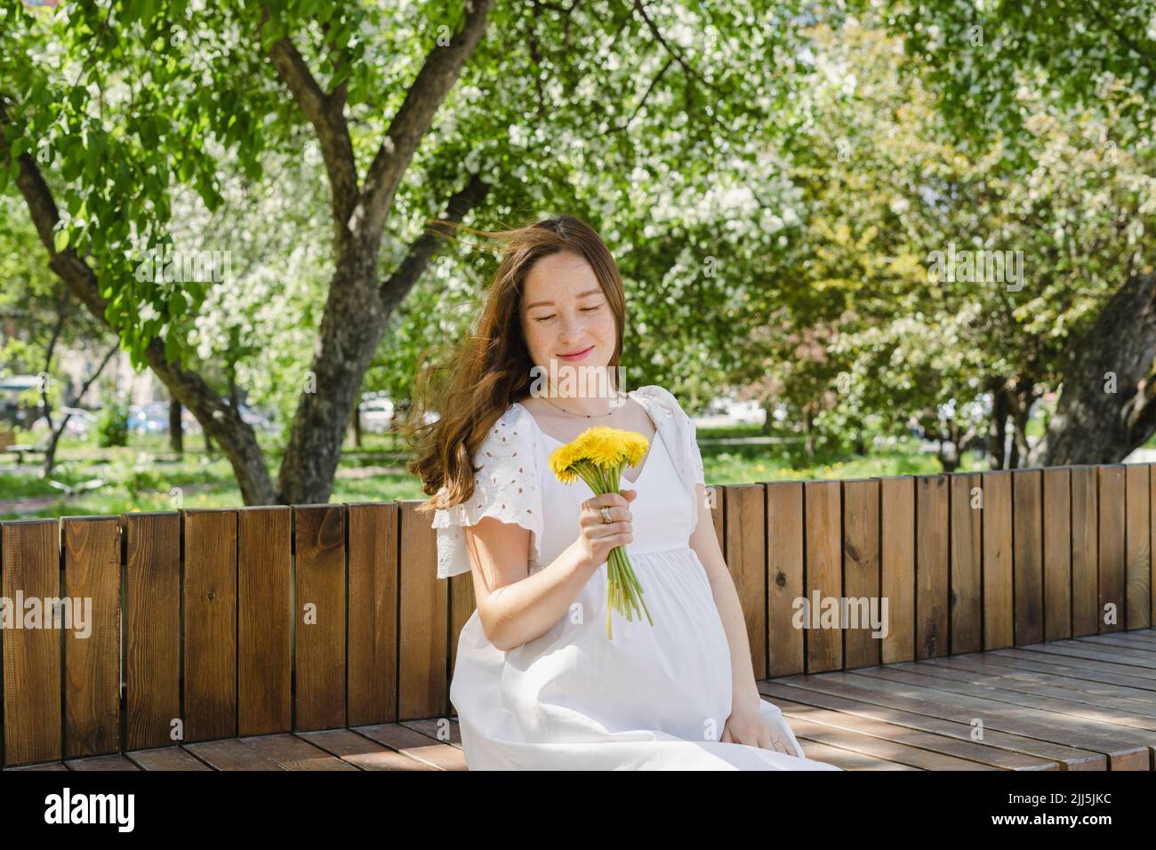 Eine Schwangerin mit Blumen sitzt im öffentlichen Park Stockfoto