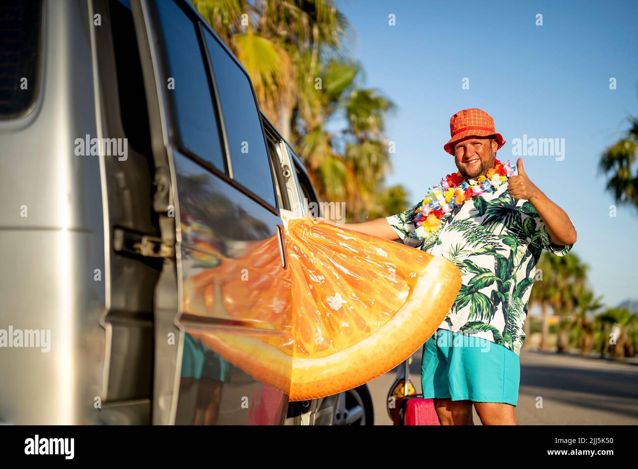 Lächelnder Mann, der ein orangefarbenes Poolfloß in den Van legte und den Daumen nach oben zeigte Stockfoto