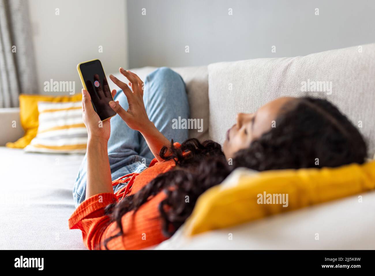 Junge Frau schaltet Smartphone aus, das zu Hause auf dem Sofa liegt Stockfoto