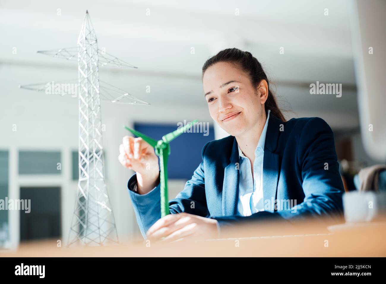 Lächelnde Geschäftsfrau, die im Büro auf die Windenergieanlage schaut Stockfoto