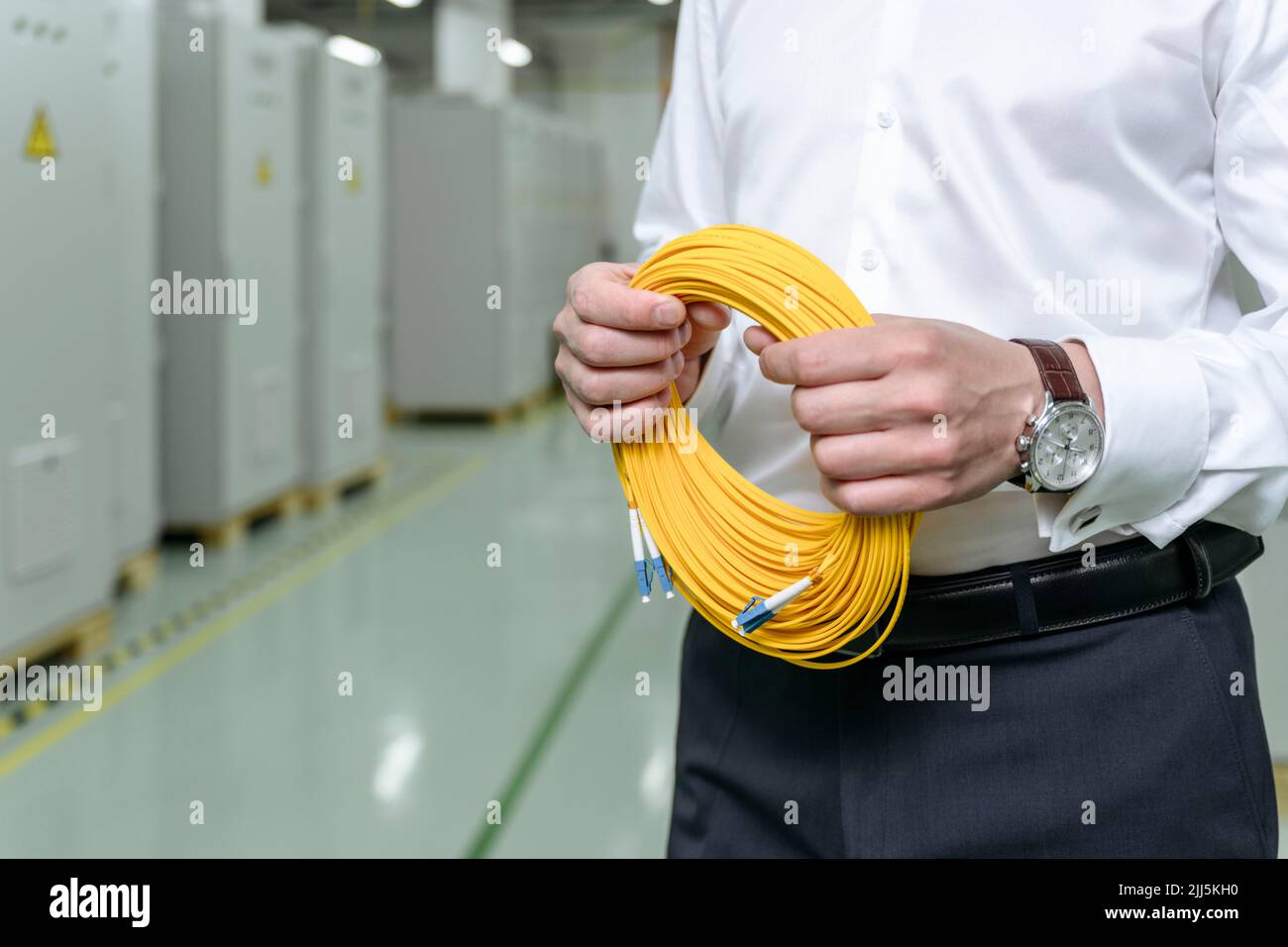Geschäftsmann hält gerollte gelbe Kabel im Werk Stockfoto
