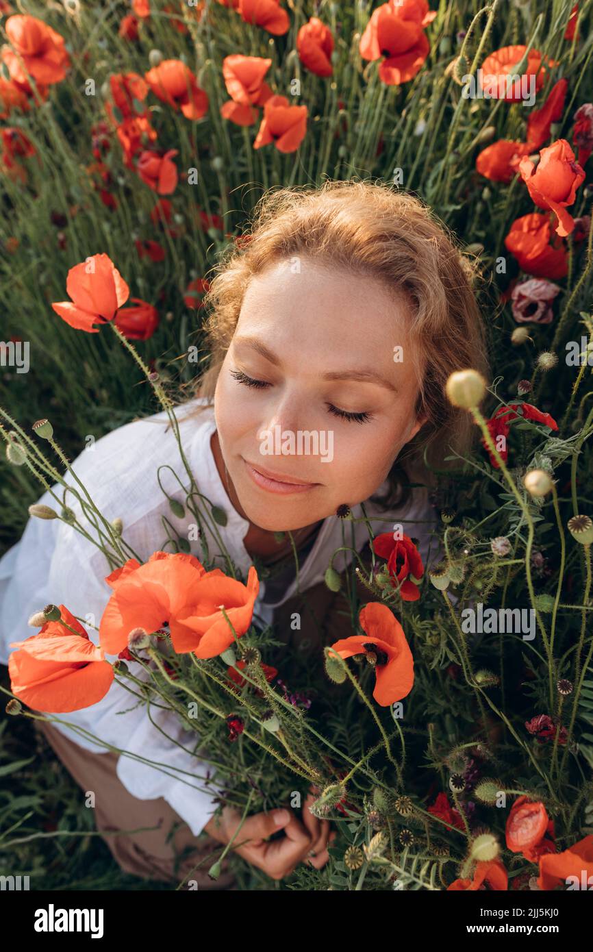 Frau mit geschlossenen Augen sitzt inmitten roter Blumen auf dem Feld Stockfoto