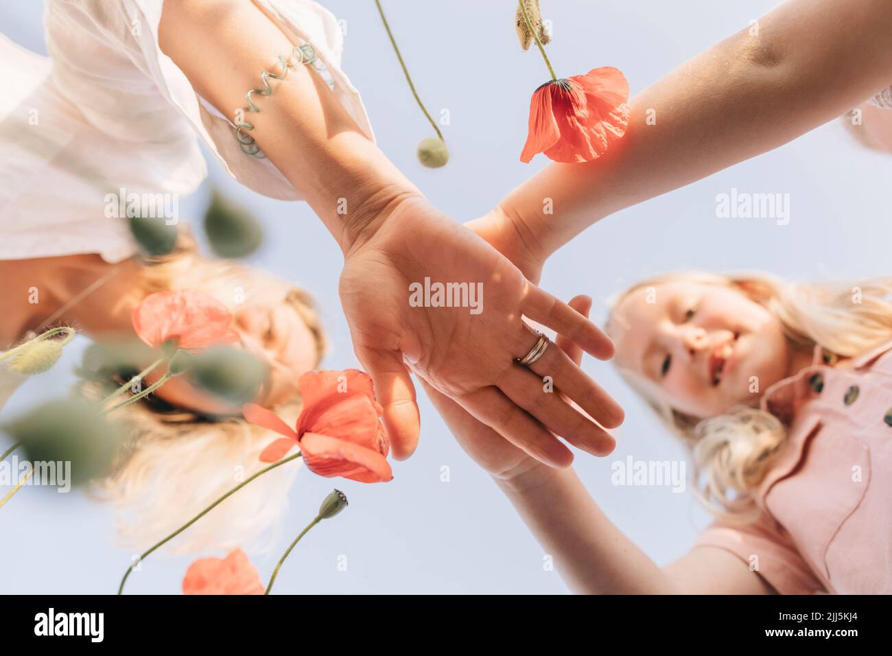 Töchter mit Mutter, die ihre Hände unter blauem Himmel stapelt Stockfoto