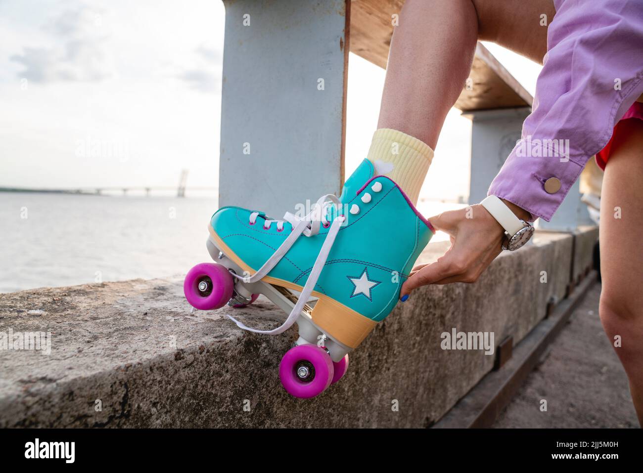 Frau, die Rollschuhe anpasst und am Geländer steht Stockfoto