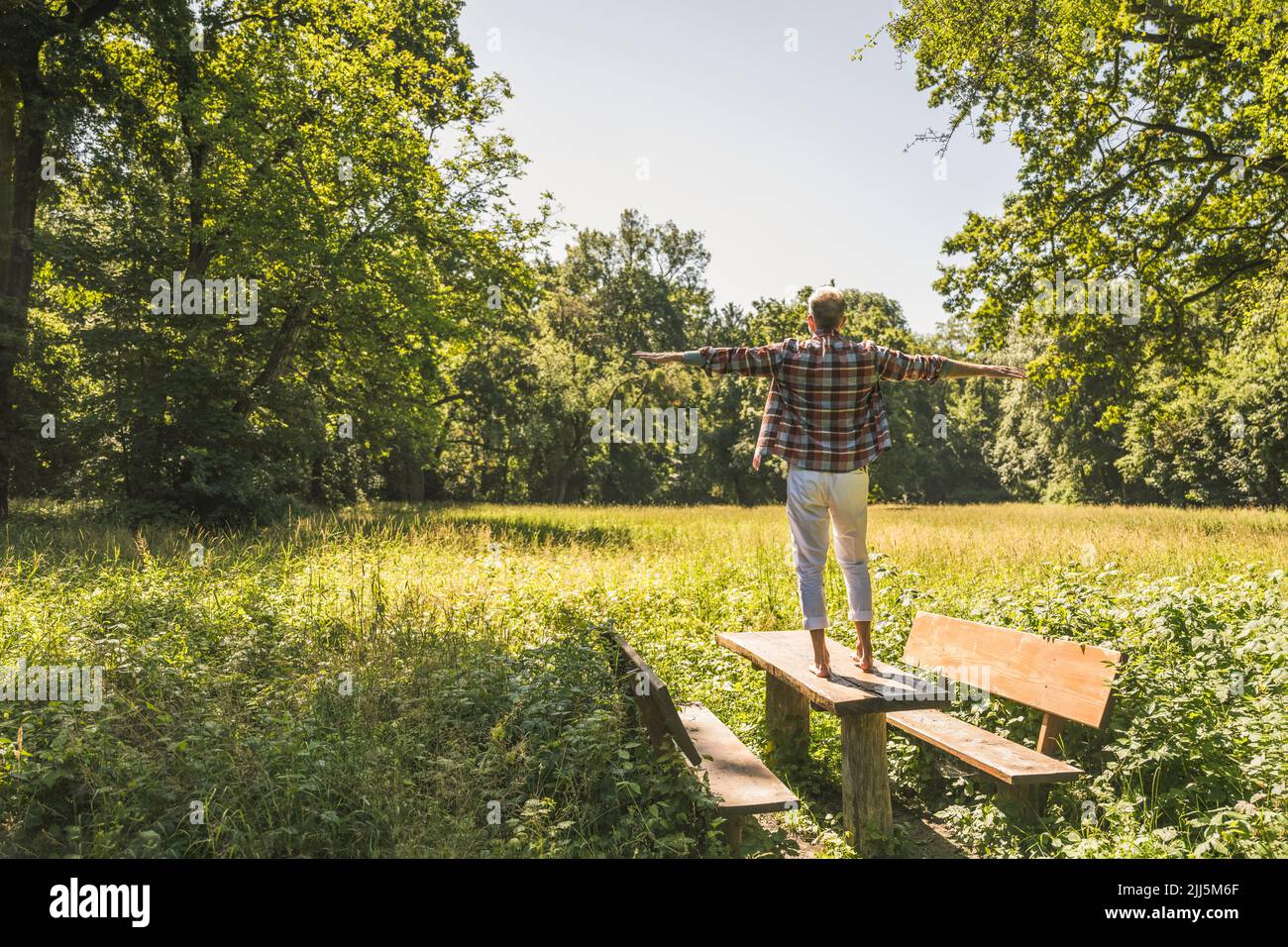 Mann mit ausgestreckten Armen, der auf dem Picknicktisch im Park steht Stockfoto