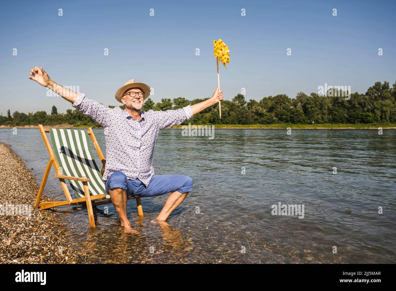 Lächelnder Mann mit ausgestreckten Armen, der am Flussufer ein Spielzeug aus Papierrad hält Stockfoto