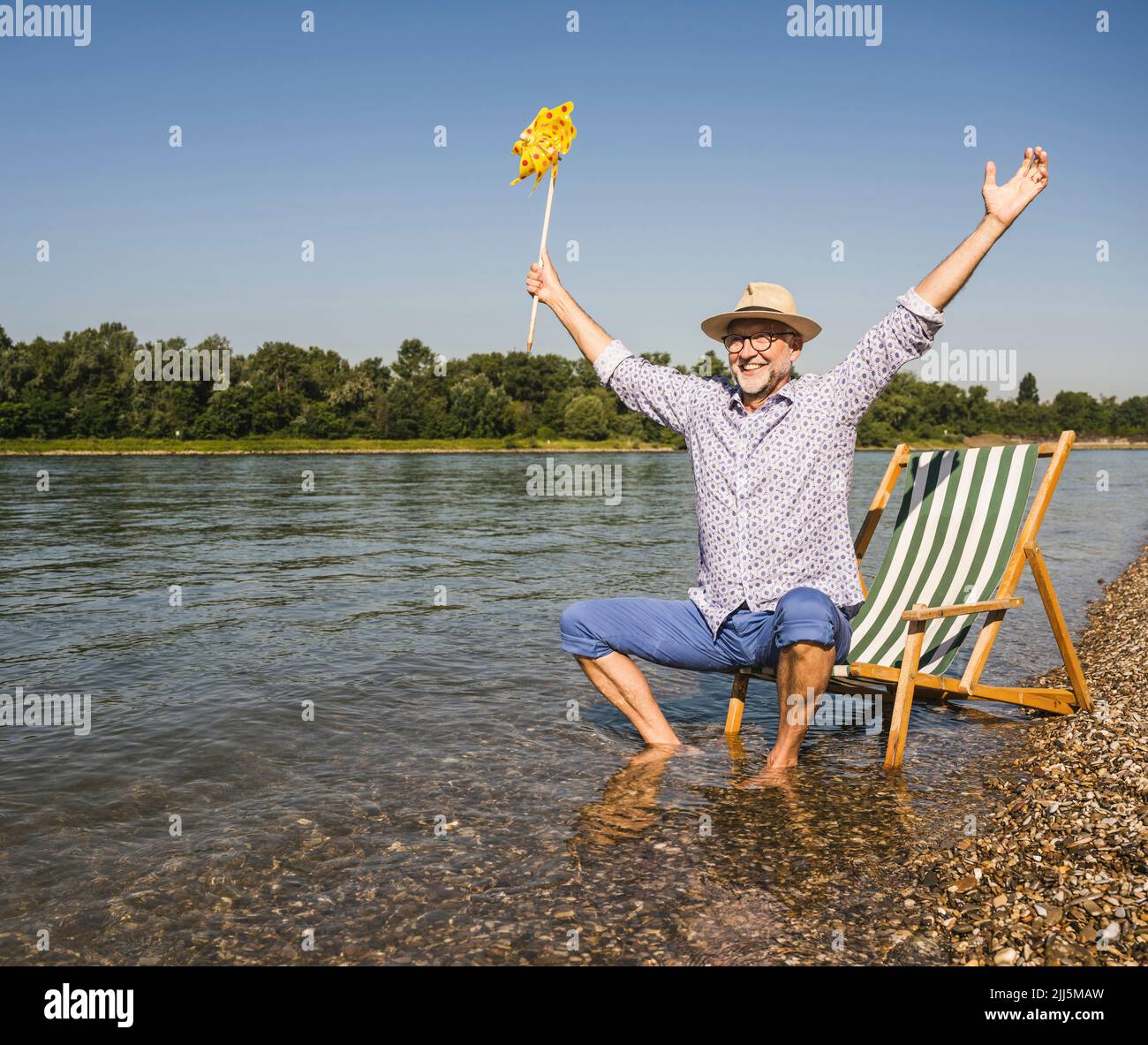 Glücklicher Mann mit ausgestreckten Armen, der am Flussufer ein Spielzeug aus Papierrad hält Stockfoto