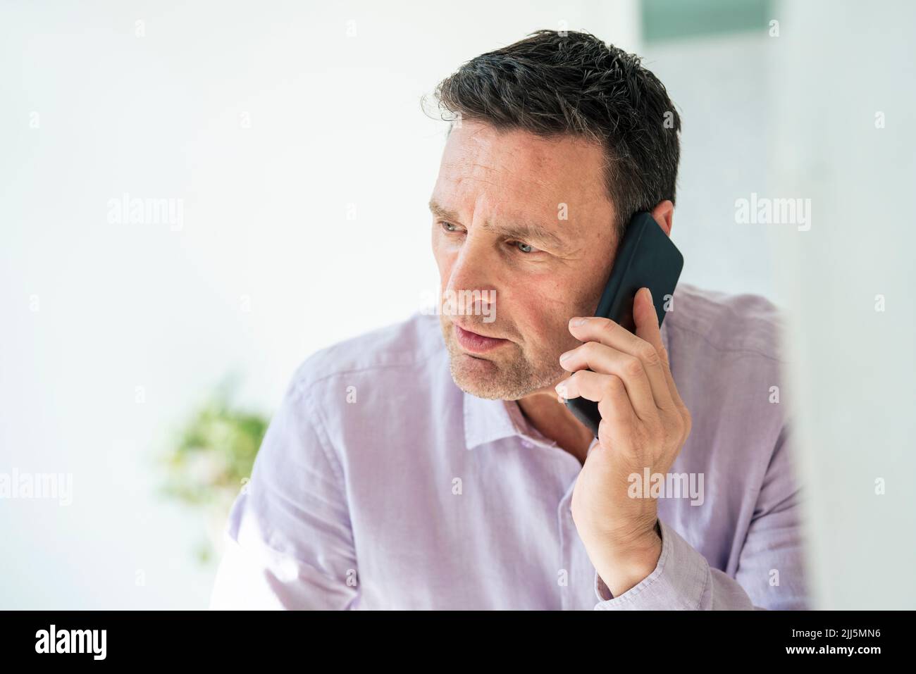 Ein reifer Geschäftsmann, der im Büro auf dem Smartphone spricht Stockfoto