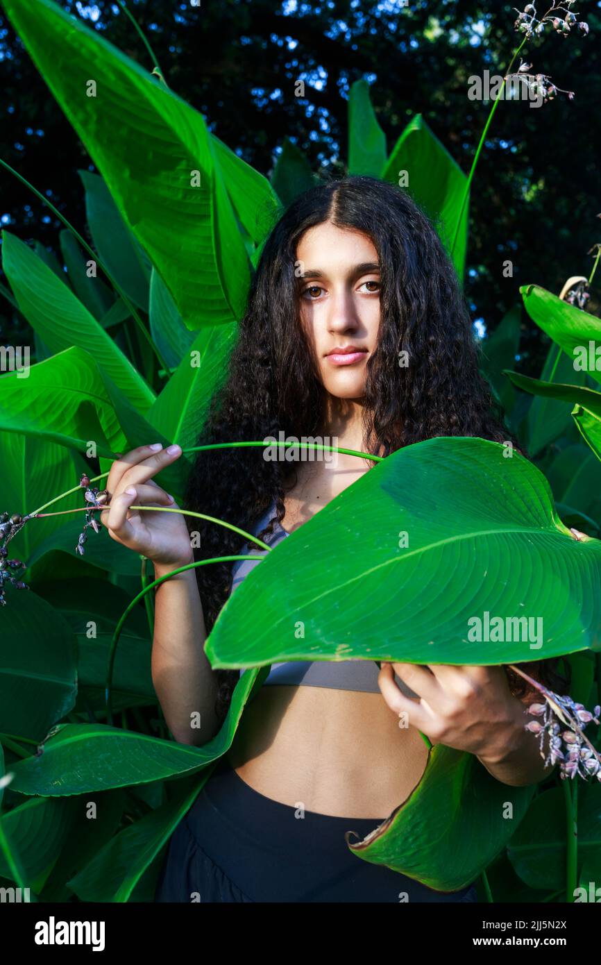 Teenagermädchen mit schwarzen Haaren, die bei Pflanzen im Park stehen Stockfoto