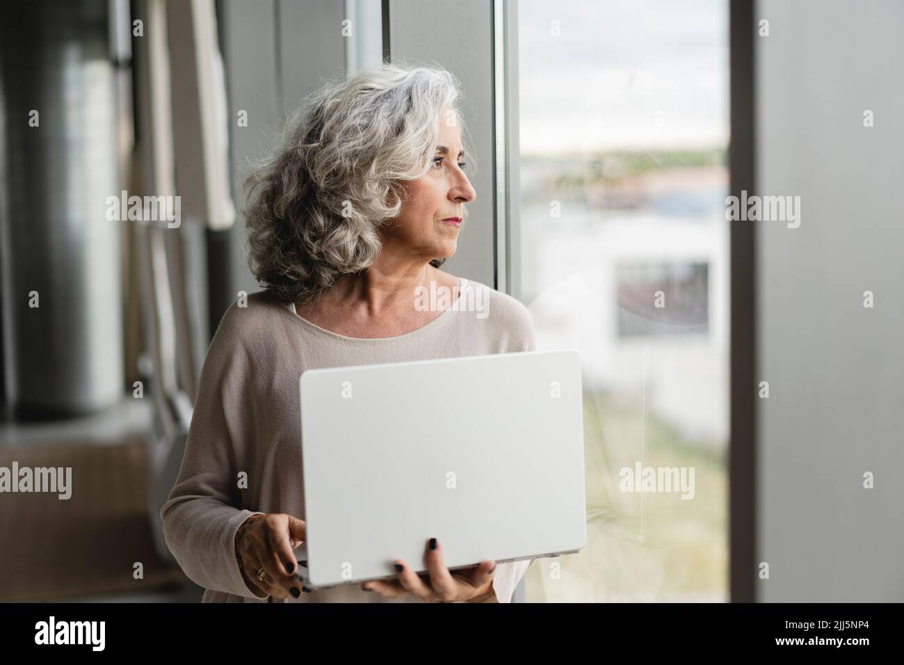 Eine Geschäftsfrau mit Laptop, die aus dem Fenster im Büro blickt Stockfoto