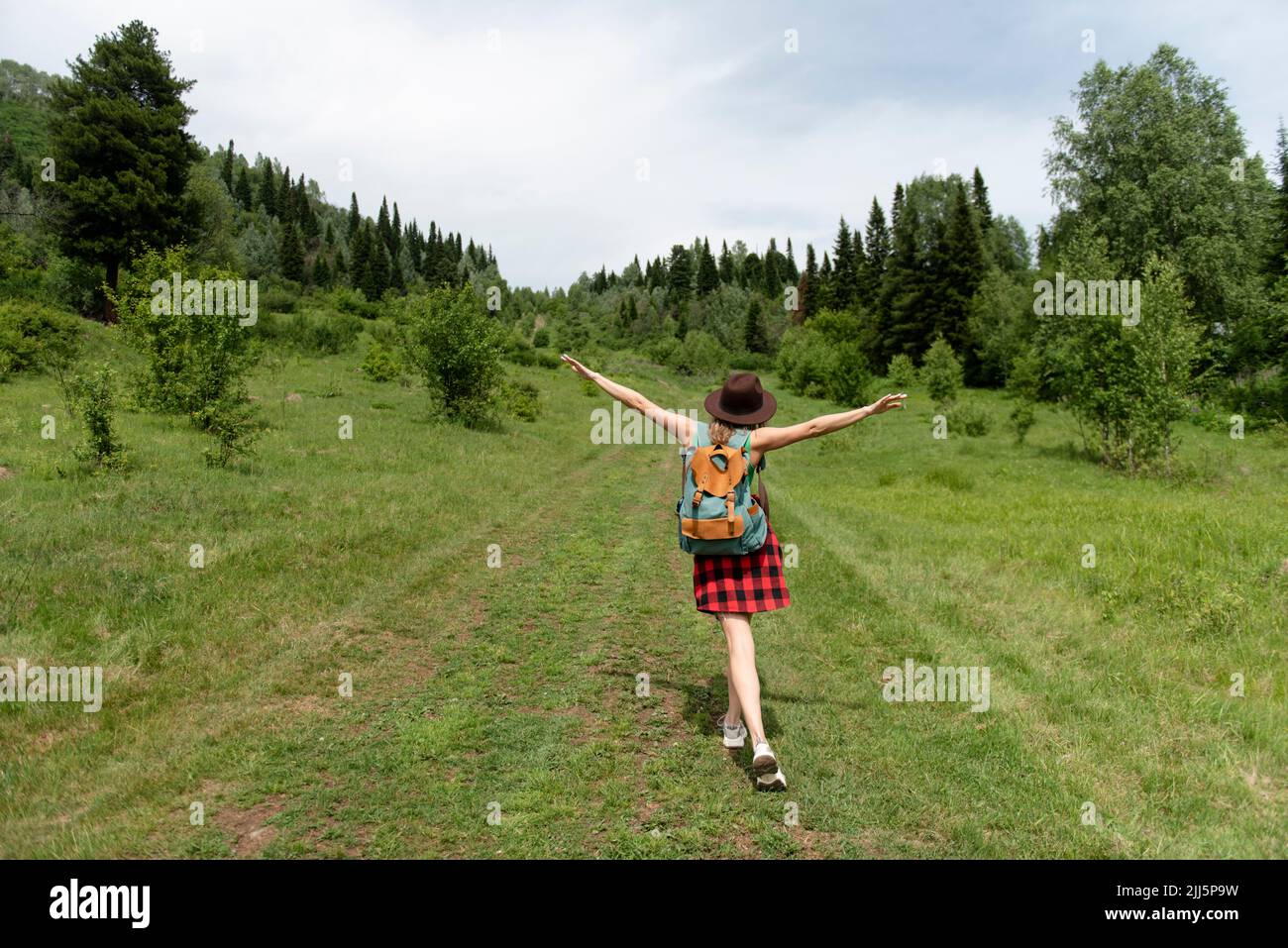 Unbeschwerte Frau mit ausgestreckten Armen auf grüner Landschaft wandern Stockfoto