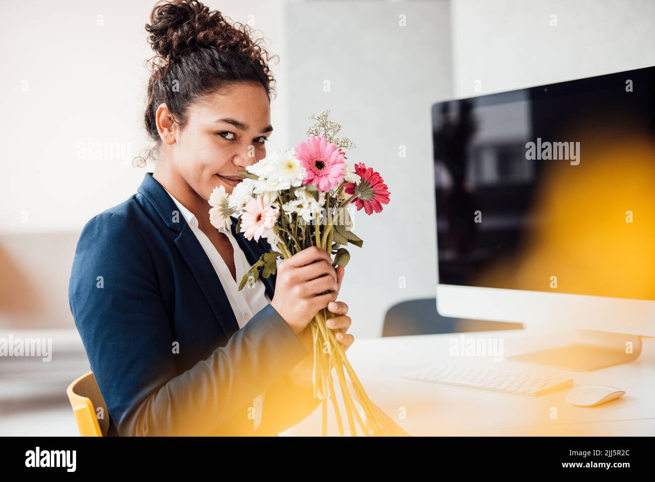 Glückliche Geschäftsfrau mit Blumen im Büro Stockfoto