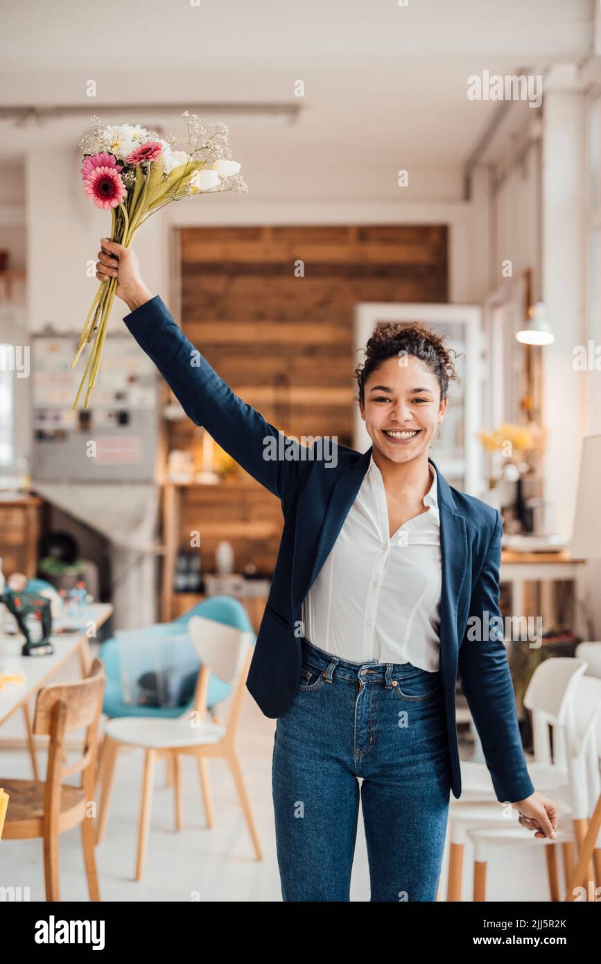 Fröhliche junge Geschäftsfrau, die mit Blumen im Büro steht Stockfoto