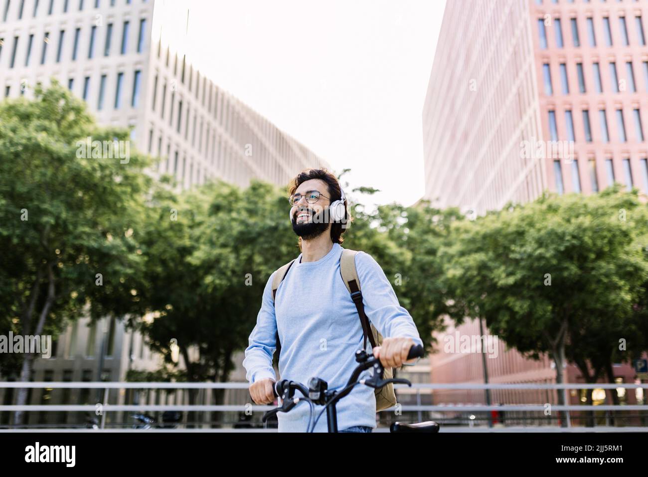 Glücklicher Mann mit kabellosen Kopfhörern, der mit dem Fahrrad steht Stockfoto