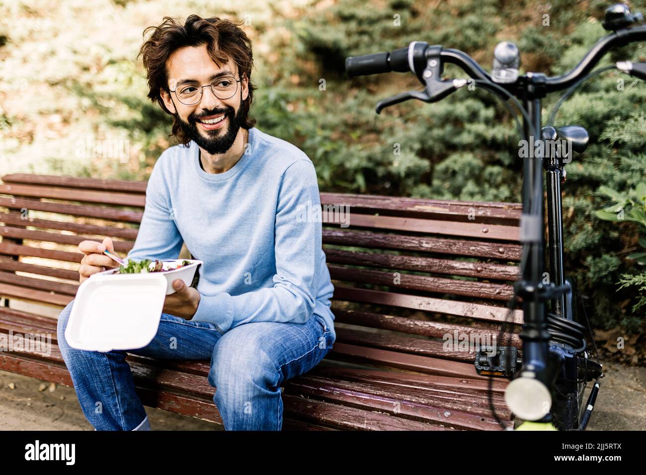 Mann mit Essen auf Parkbank sitzend und Fahrrad angeschaut Stockfoto