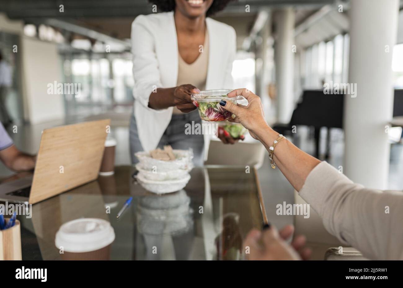 Eine Geschäftsfrau gab einem älteren Kollegen an der Rezeption eine Salatbox Stockfoto