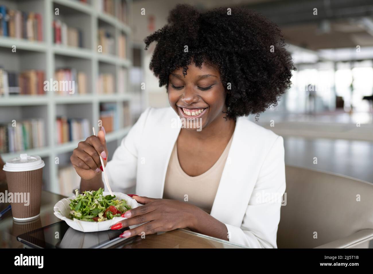 Eine glückliche Geschäftsfrau, die an der Rezeption im Büro Salat isst Stockfoto