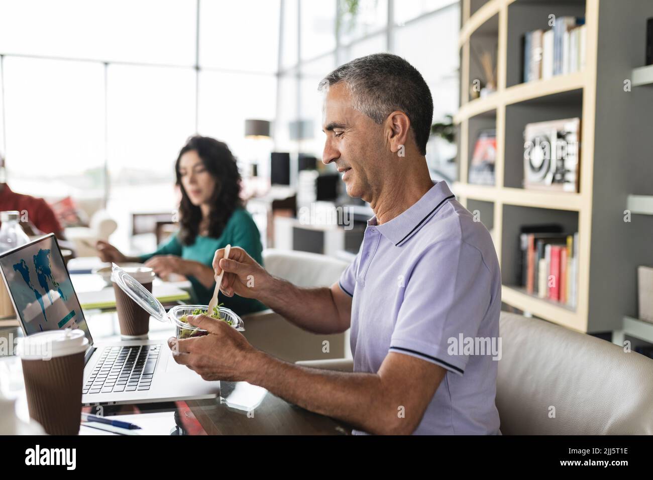 Ein glücklicher Geschäftsmann, der an der Rezeption Salat isst Stockfoto