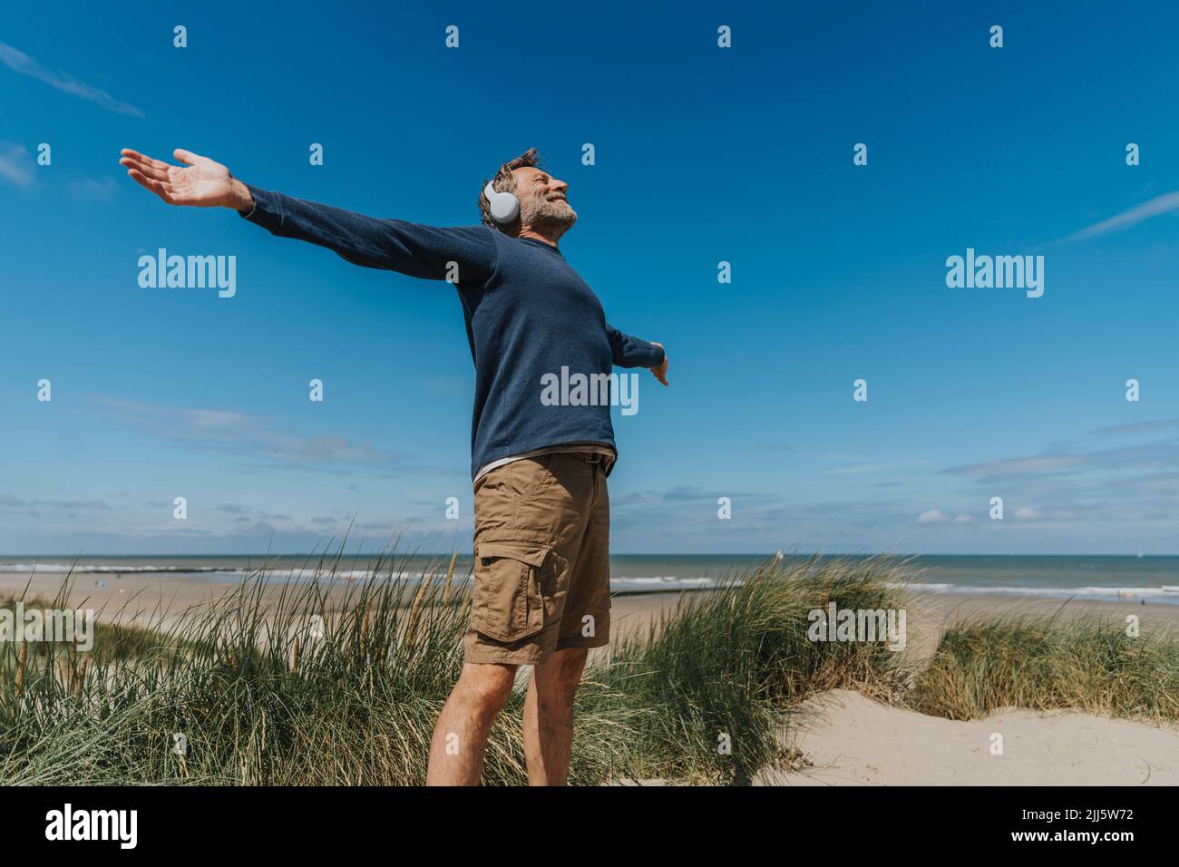 Glücklicher Mann mit ausgestreckten Armen, der am Strand steht Stockfoto