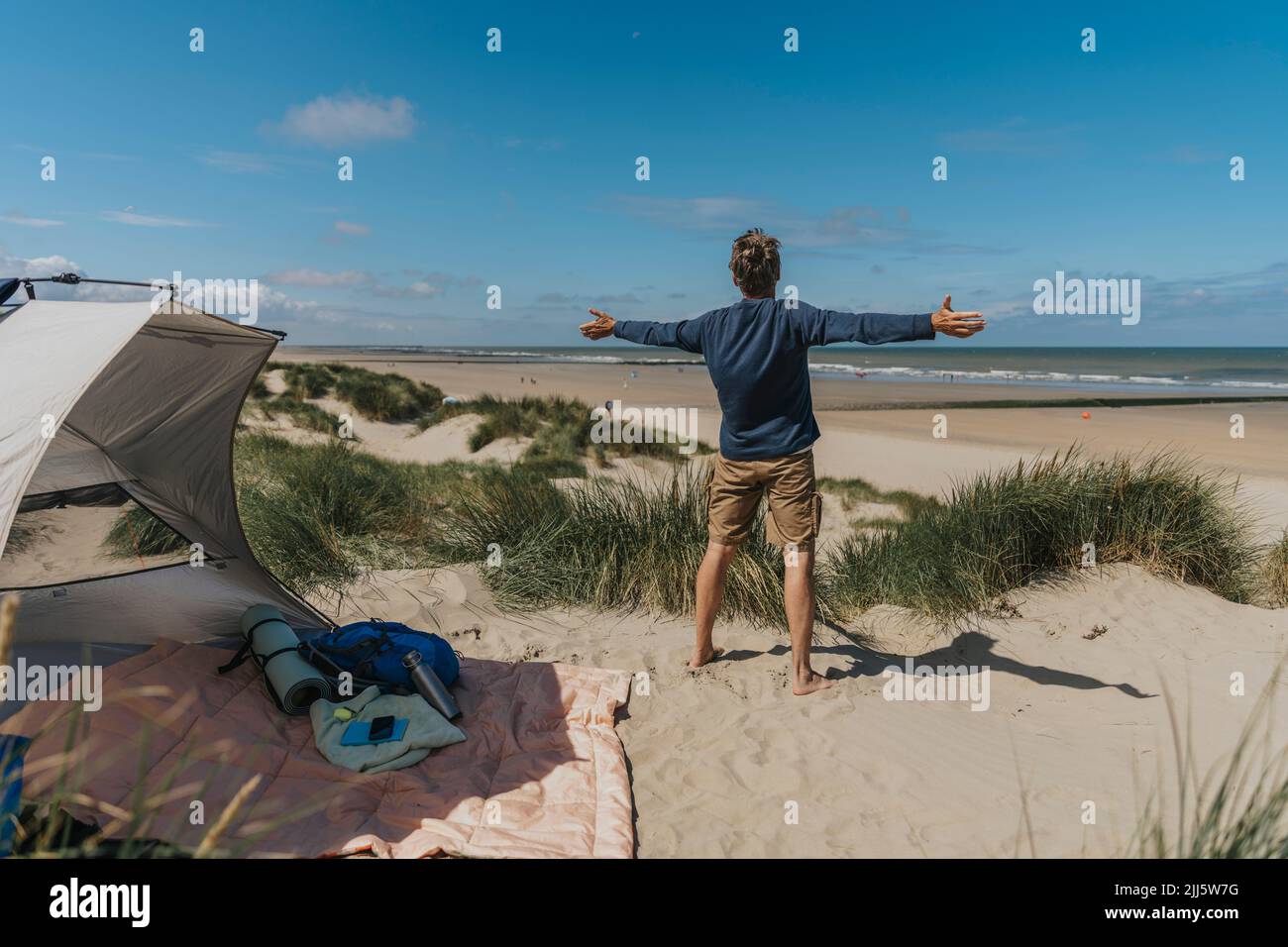 Reifer Mann mit ausgestreckten Armen, der am Strand steht Stockfoto