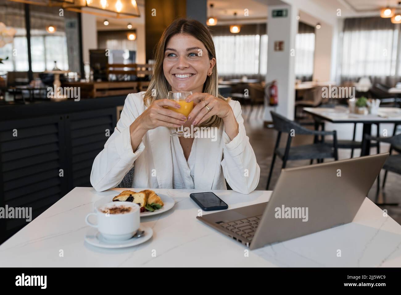 Lächelnde Geschäftsfrau mit Saftglas und Laptop im Restaurant Stockfoto