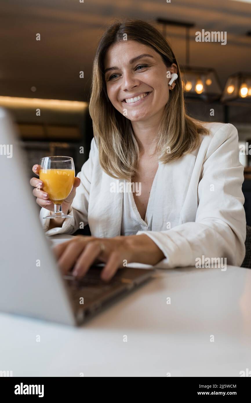 Lächelnde Geschäftsfrau mit Saftglas am Laptop im Restaurant Stockfoto