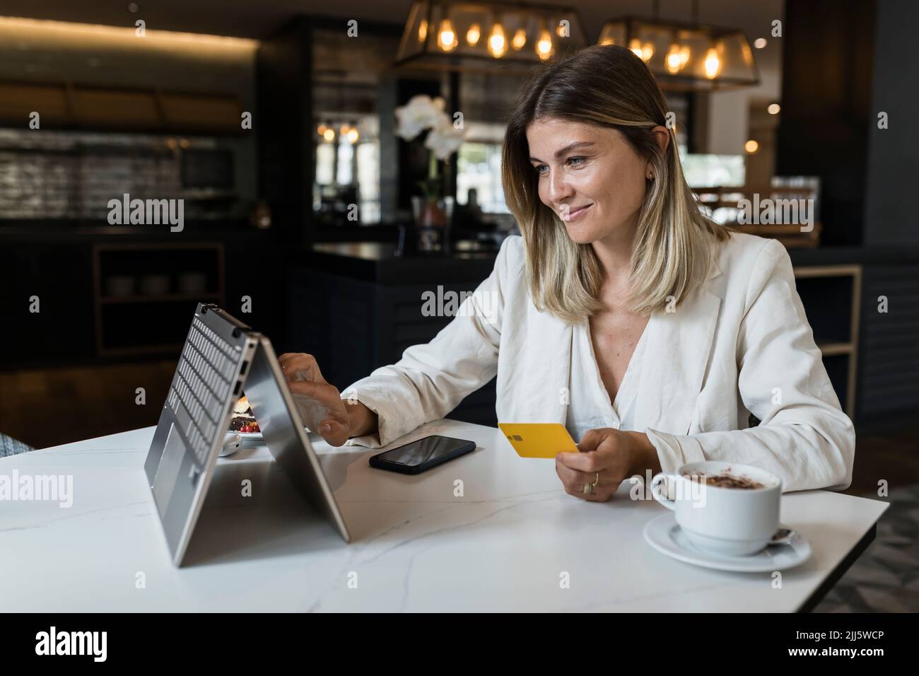 Lächelnde Geschäftsfrau mit Kreditkarte beim Online-Shopping über den Laptop im Restaurant Stockfoto