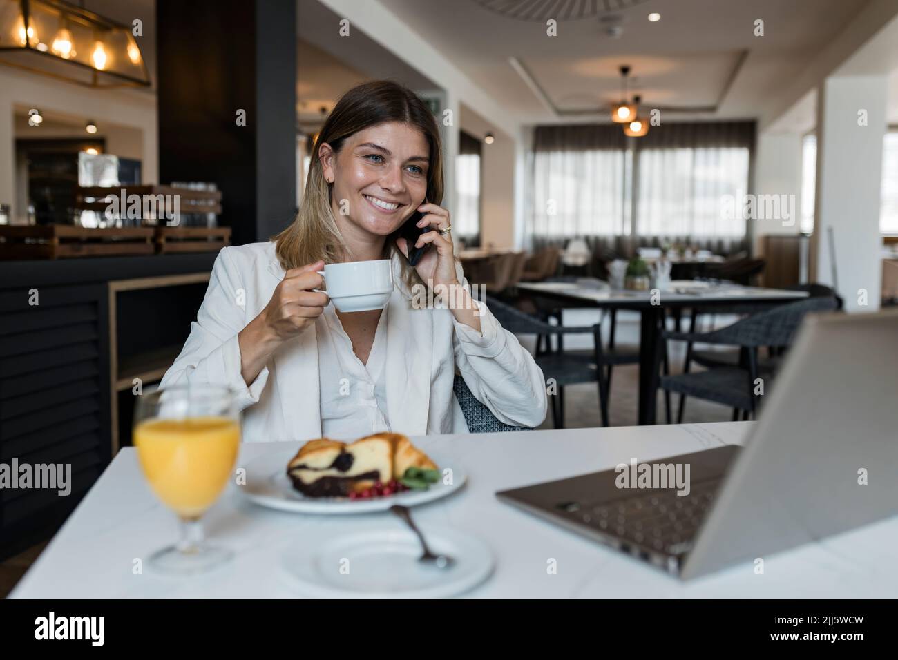 Lächelnde Geschäftsfrau mit Kaffeetasse im Restaurant, die mit dem Mobiltelefon spricht Stockfoto