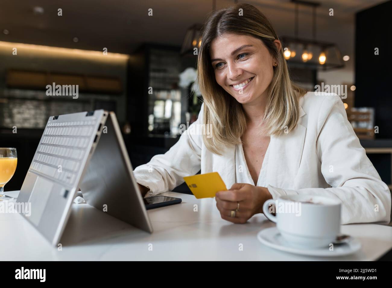 Glückliche Geschäftsfrau mit Kreditkarte beim Online-Shopping über Laptop im Restaurant Stockfoto