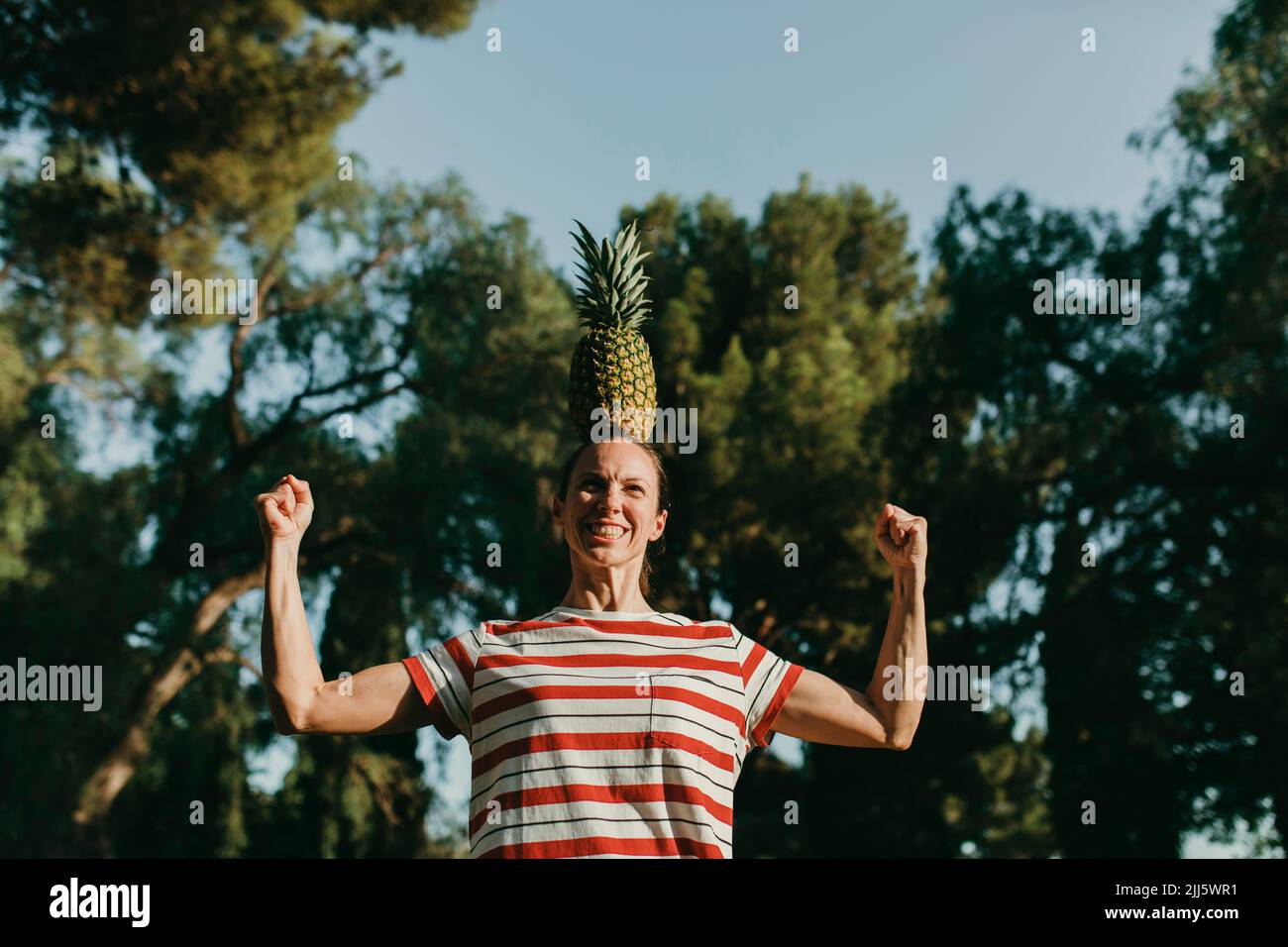 Frau balanciert Ananas auf dem Kopf und beugt Muskeln im Park Stockfoto