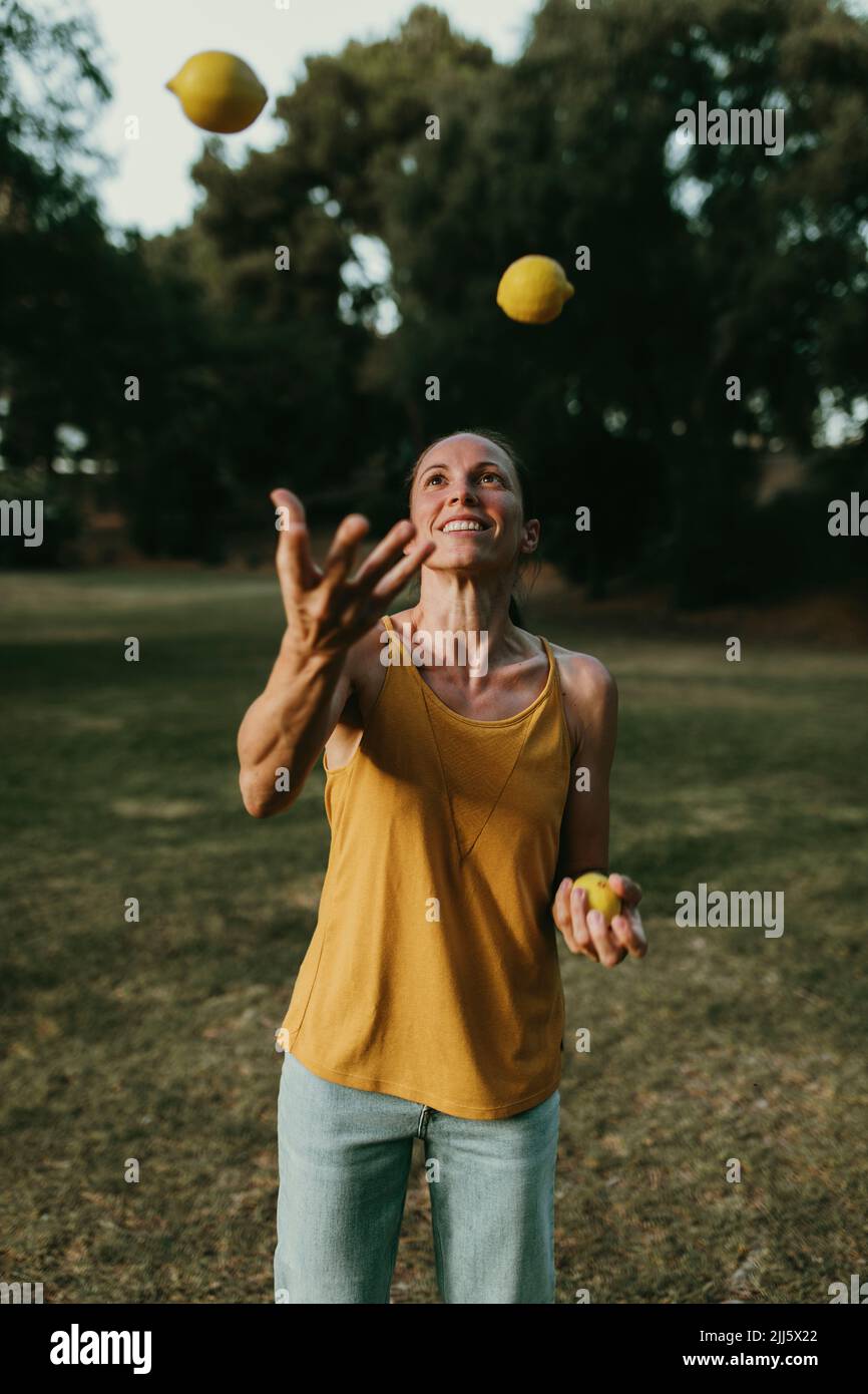 Lächelnde Frau jongliert Zitronen im Park Stockfoto