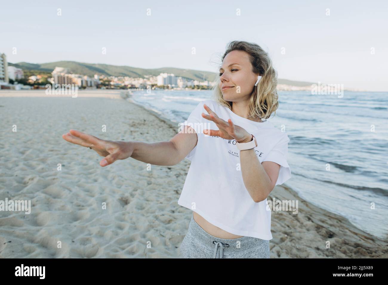 Fröhliche Frau mit kabellosen in-Ear-Kopfhörern, die am Strand tanzt Stockfoto