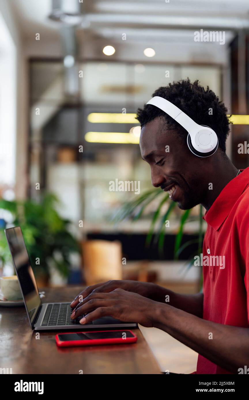 Lächelnder Mann mit kabellosen Kopfhörern am Laptop Stockfoto