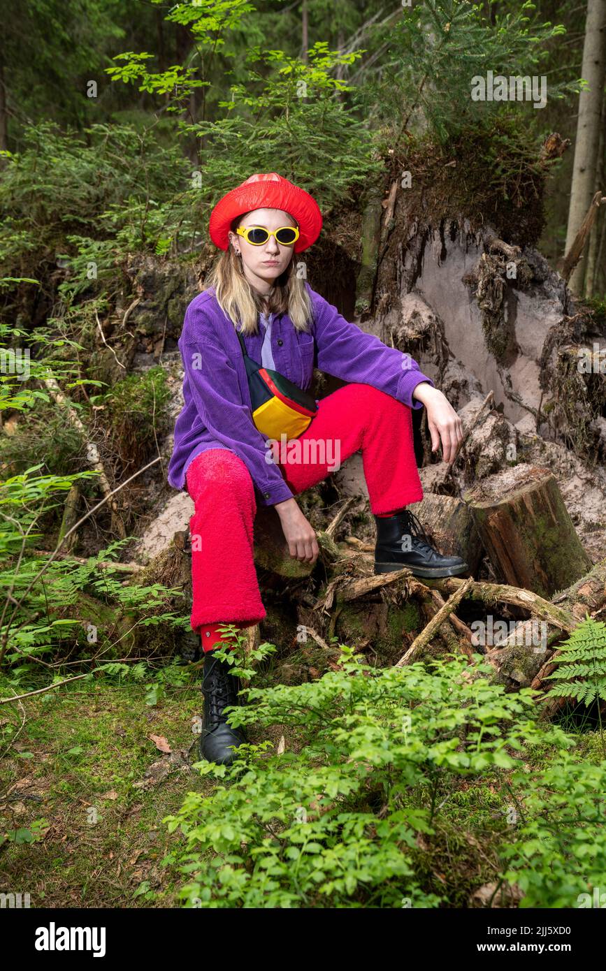 Frau mit Sonnenbrille auf Baumstumpf sitzend Stockfoto