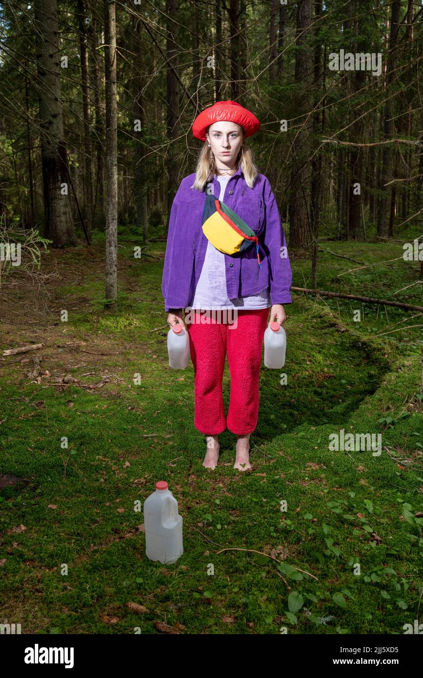 Frau mit Hut und Gallonen-Containern, die am Wald stehen Stockfoto