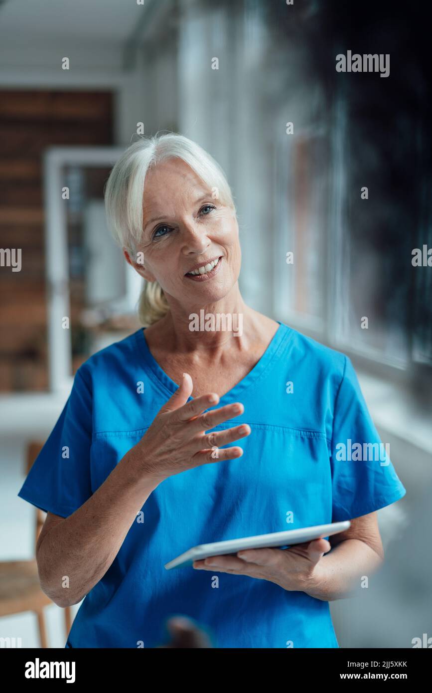 Lächelnde Krankenschwester, die den Tablet-PC gestikuliert hält Stockfoto