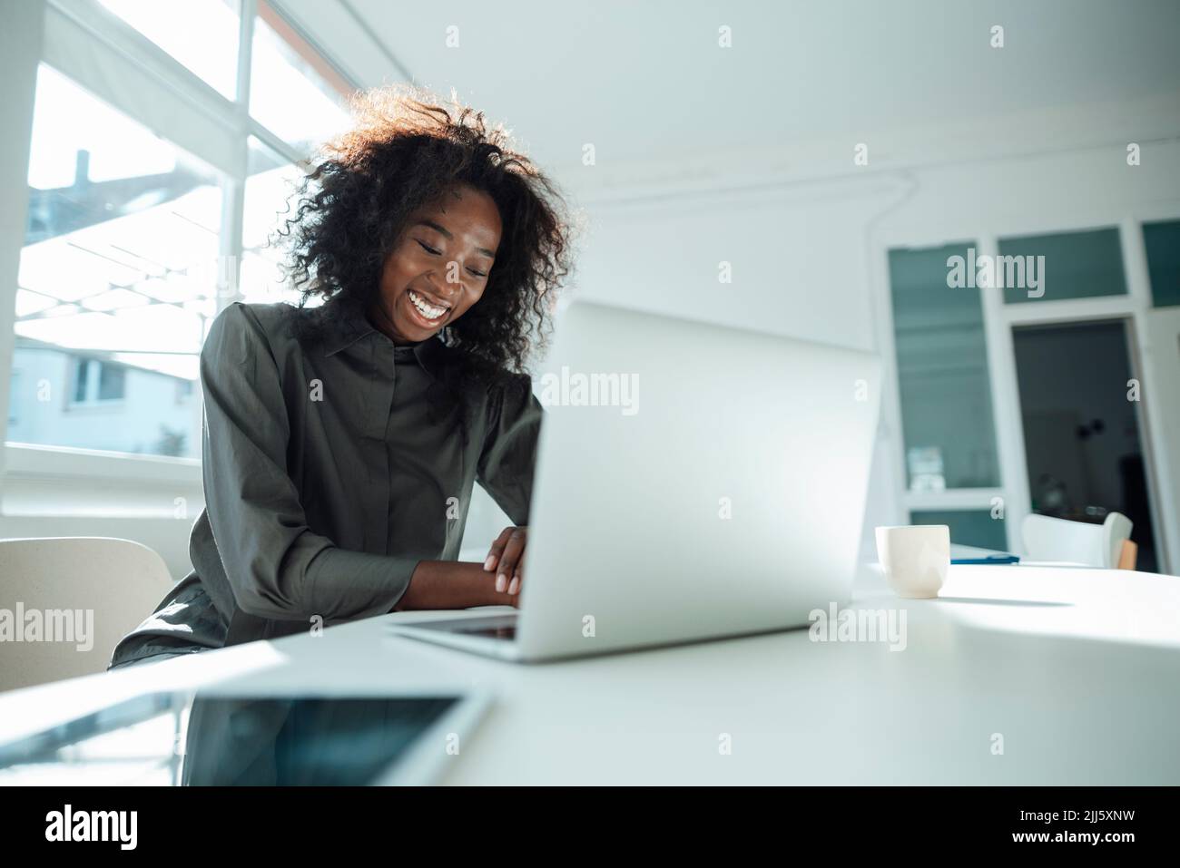 Glückliche Geschäftsfrau, die mit einem Laptop am Schreibtisch im Büro sitzt Stockfoto