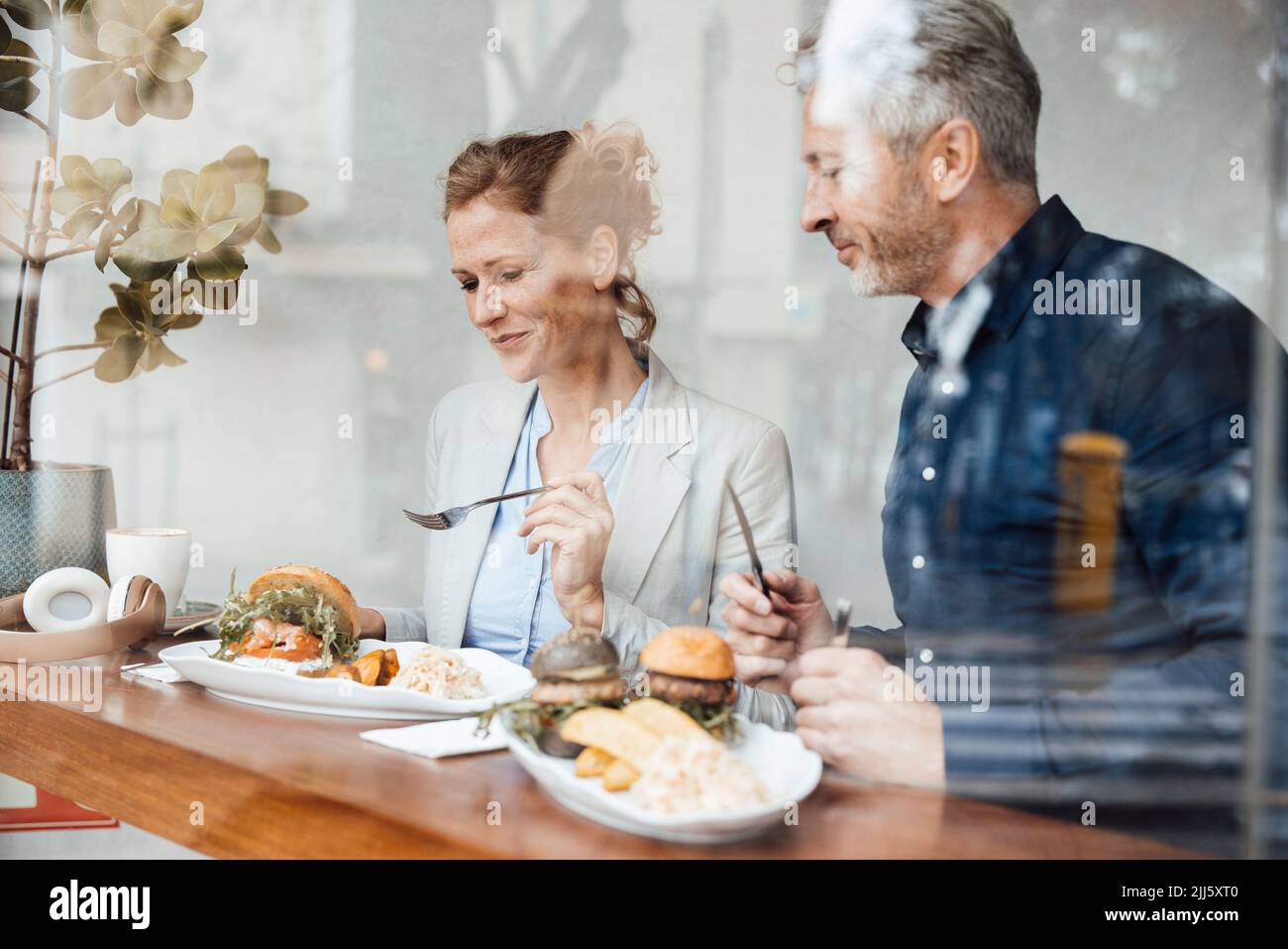 Lächelnde Geschäftsfrau mit Geschäftsmann, der im Café durch Glas gesehen zu Mittag gegessen hat Stockfoto