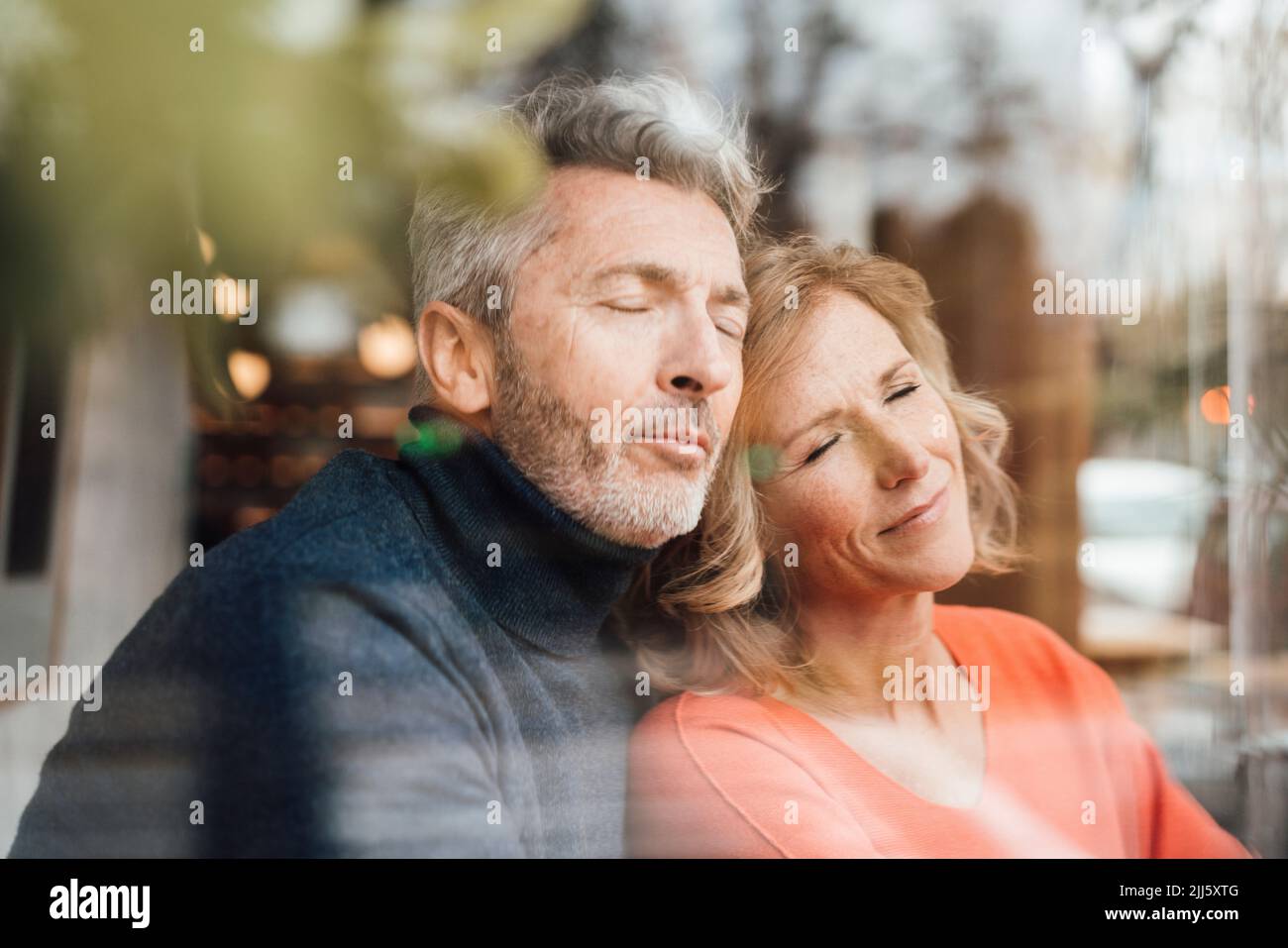 Paar mit geschlossenen Augen im Café durch Glas gesehen Stockfoto