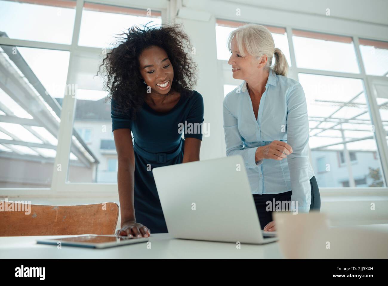 Lächelnde Geschäftsfrauen diskutieren über den Laptop am Schreibtisch im Büro Stockfoto
