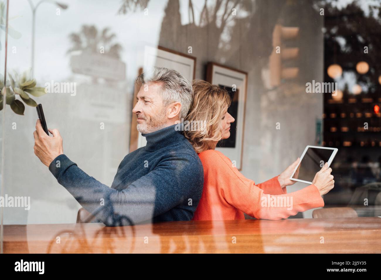 Lächelndes Paar, das drahtlose Technologien verwendet, sitzendes Café, das durch das Glas gesehen wird Stockfoto