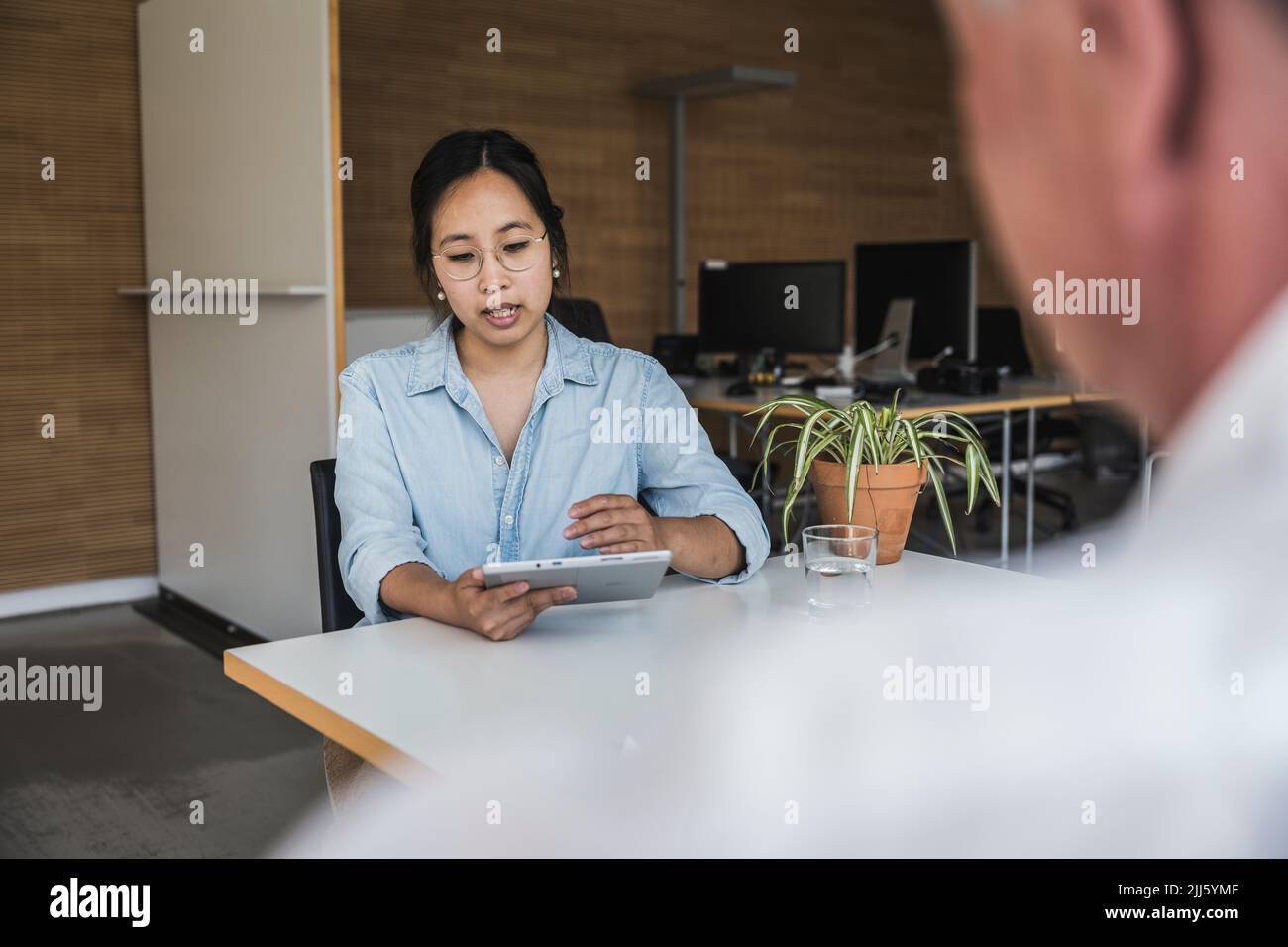 Geschäftsfrau, die einen Tablet-PC nutzt und mit Kollegen am Schreibtisch über die Arbeit spricht Stockfoto