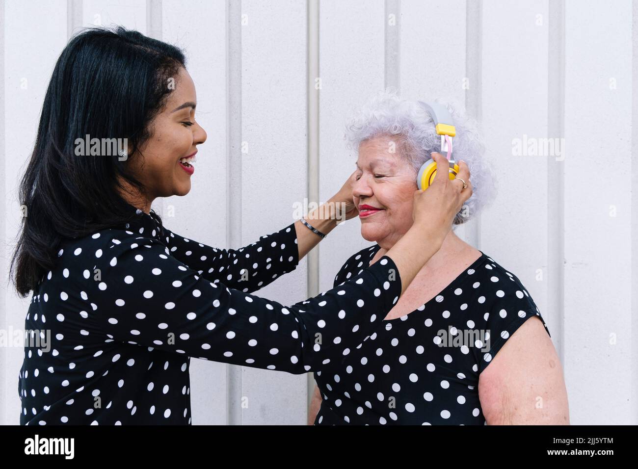 Tochter hilft Mutter, kabellose Kopfhörer zu tragen Stockfoto