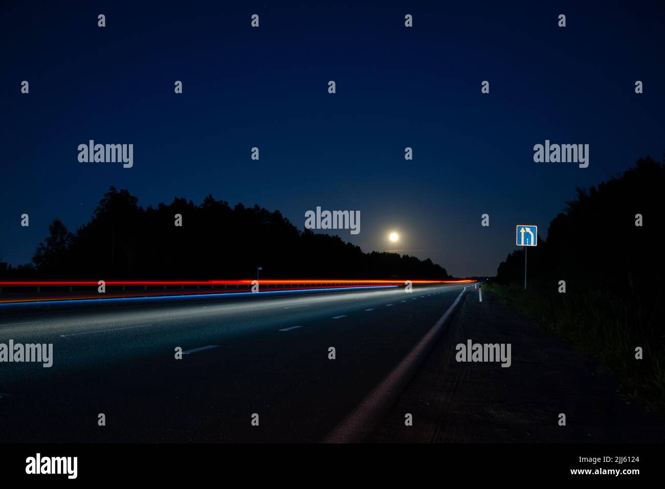Eine Nachtspur mit einem Mond und verschwommenen Lichtern aus den Scheinwerfern von Autos.lange Belichtungszeit Stockfoto