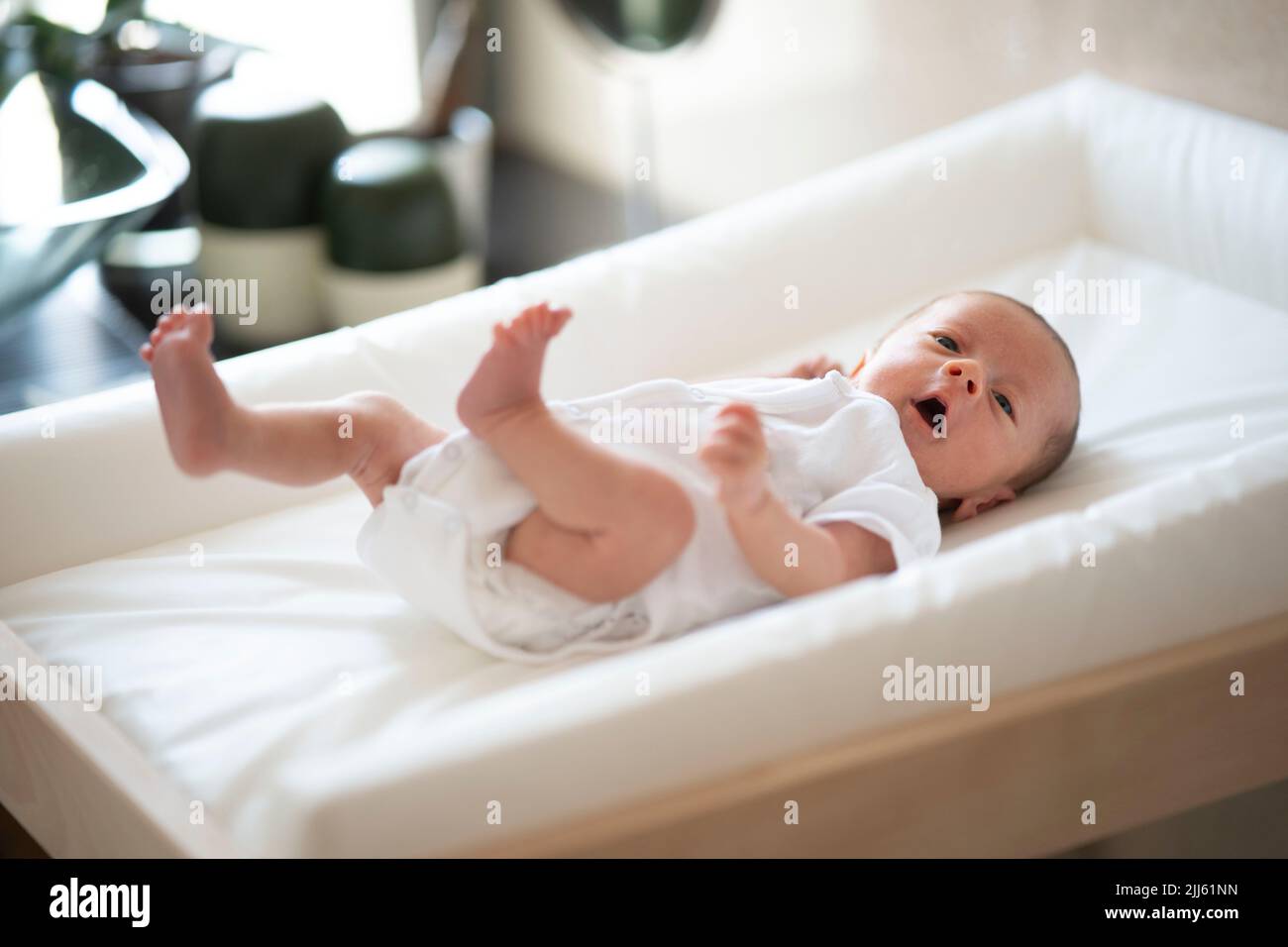 Aufgewütteltes Baby, das Arme und Beine winkt, während es auf dem Windelwechsler liegt Stockfoto