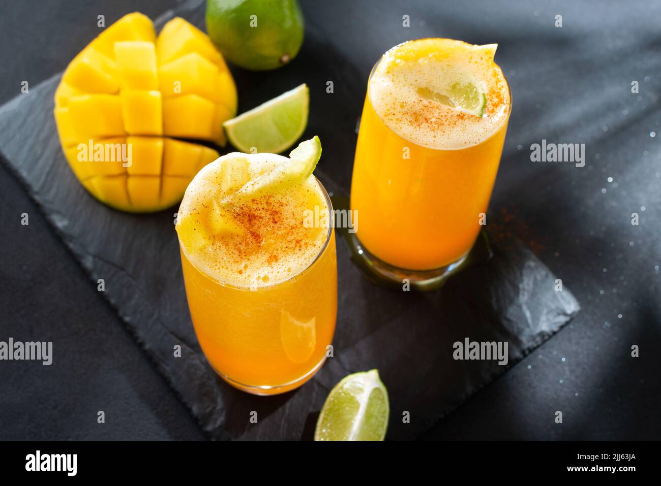 Mangonada-mexikanischer Mango-Smoothie mit Chamoy-Sauce und Chili-Limette-Würze und Tamarindenbonbons. Zwei Mangonada-Sommercocktails im Dunkeln Stockfoto